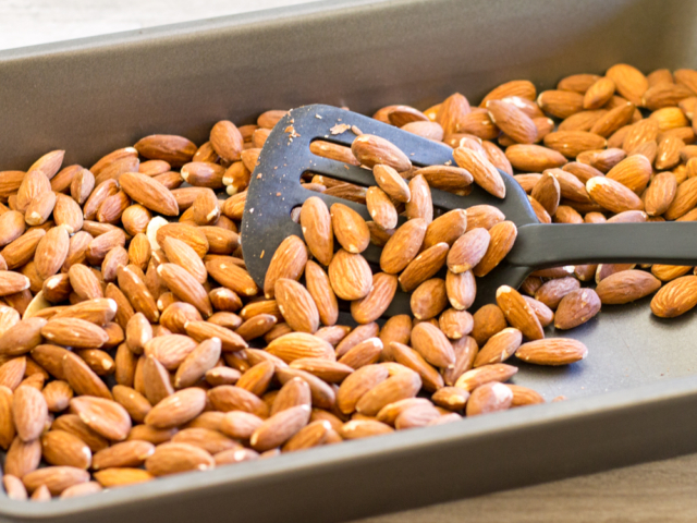Almonds spread out in cake pan for dry roasting in oven