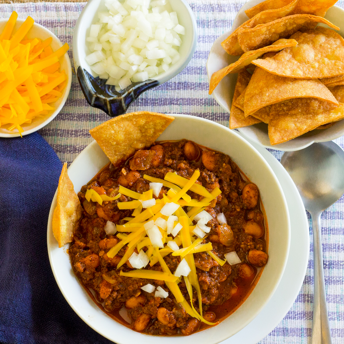 Bowl of vegetarian chili with onions, cheese and homemade corn chips