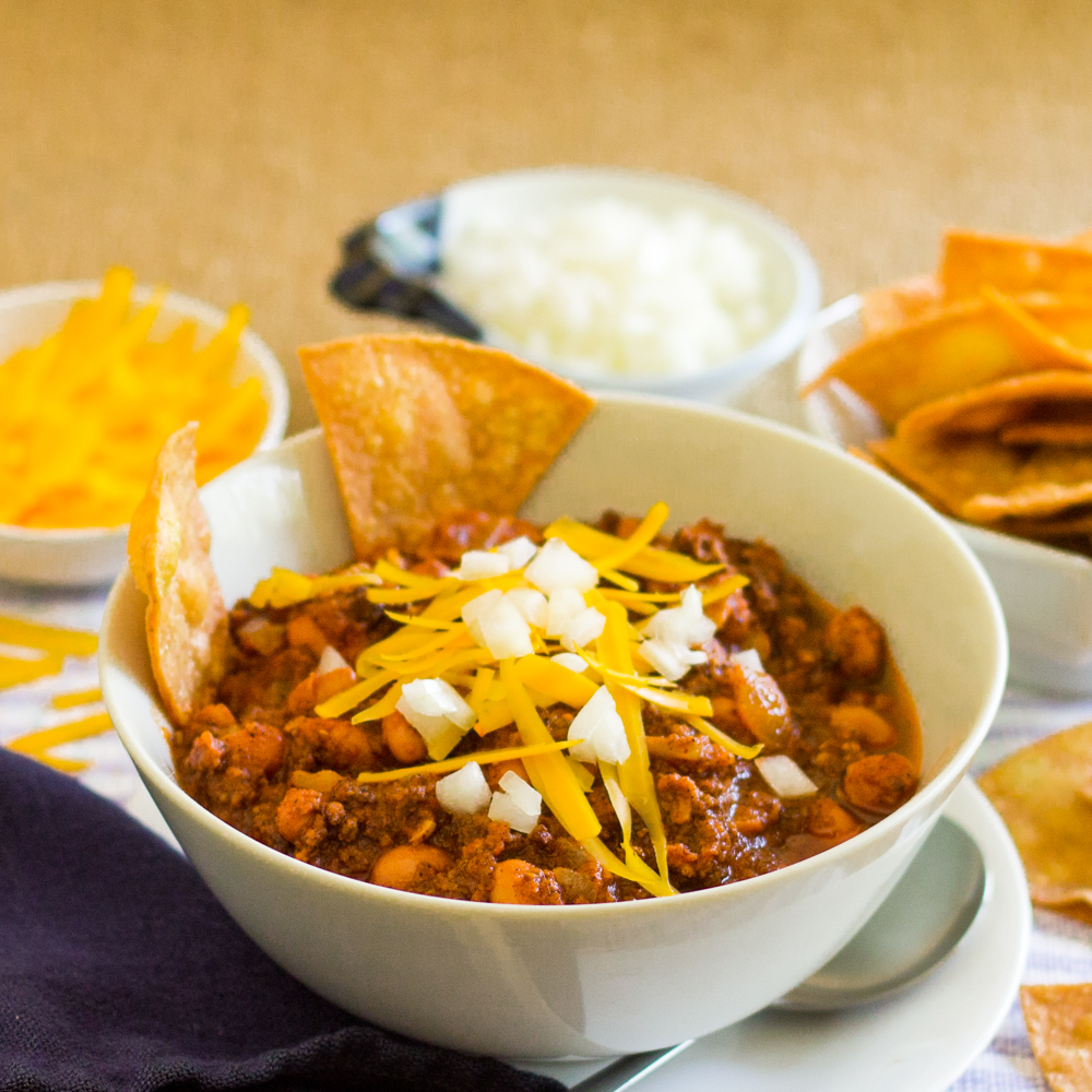 Bowl of vegetarian chili with onions, cheese and homemade corn chips