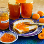 Apricot jam spread on fresh bread with jars of jam