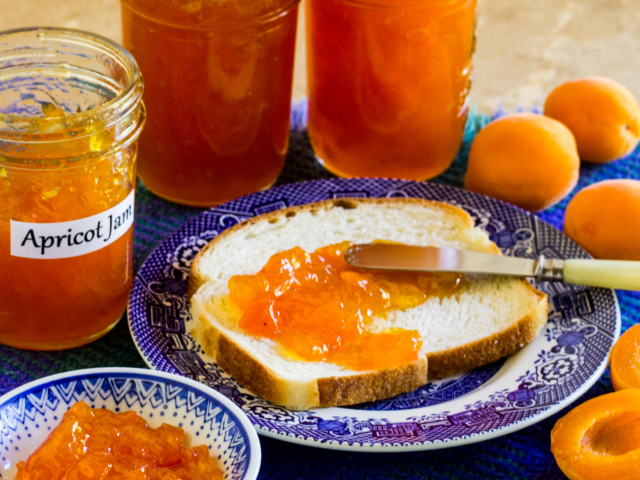 Apricot jam spread on fresh bread with jars of jam