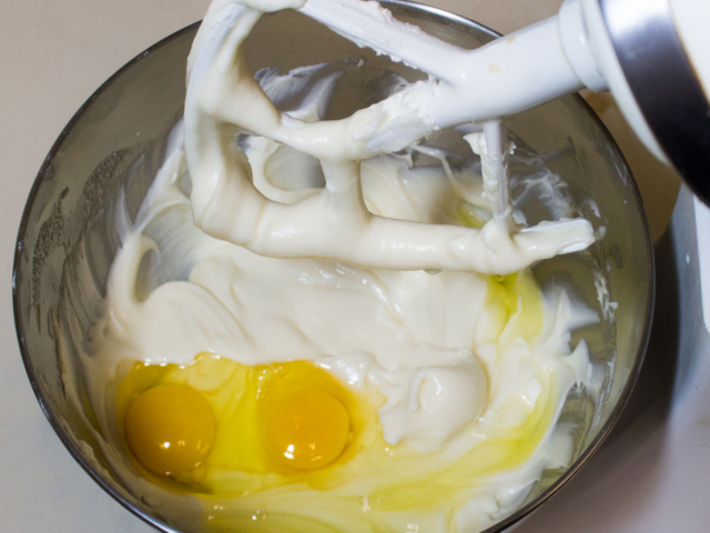Two eggs added to beaten cream cheese and sugar in mixing bowl.