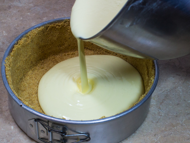 Cream cheese filling being poured into Graham cracker crust. Bake at 325° for 65 minutes.