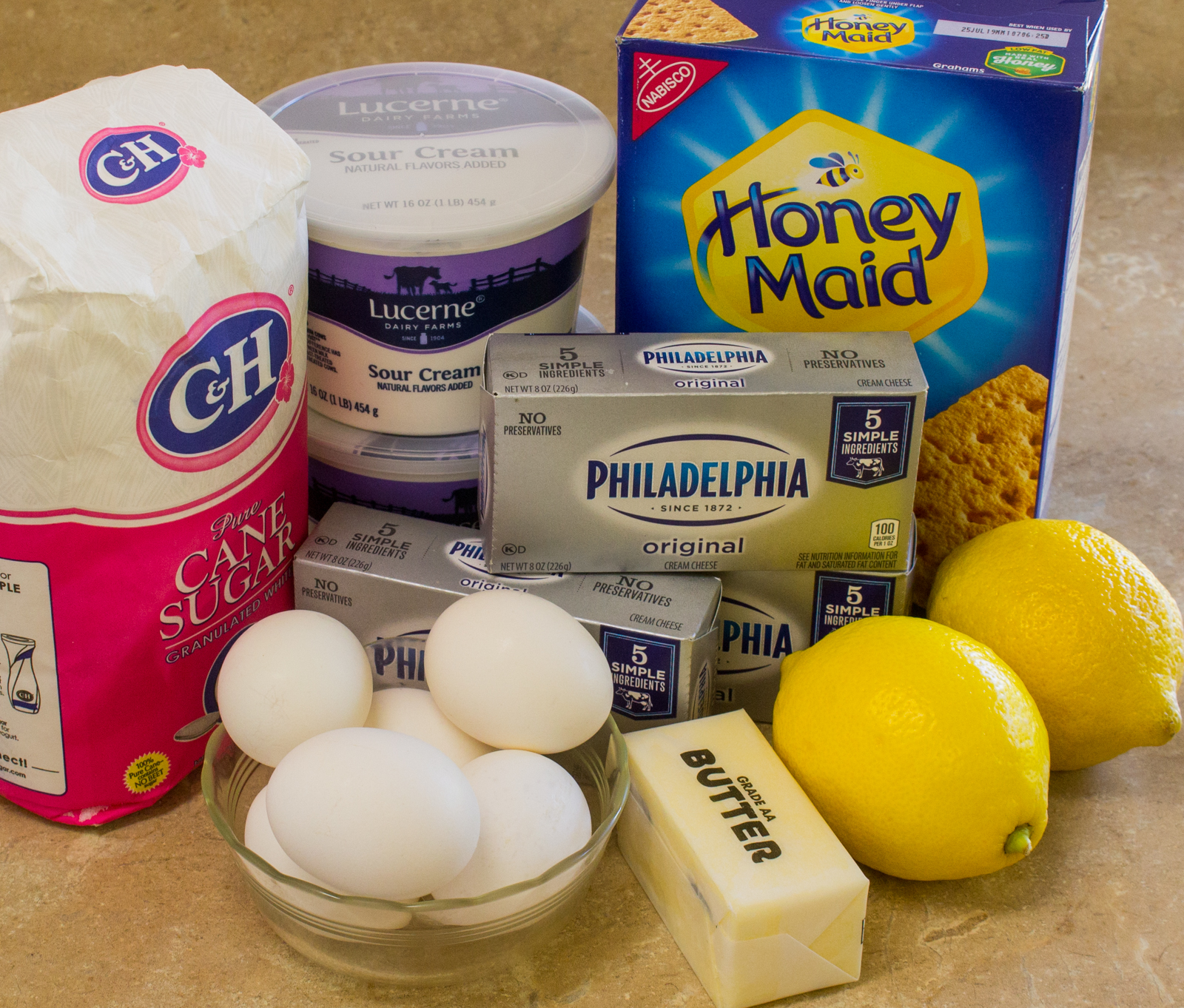 Basic Ingredients for New York Cheesecake with lemon, sugar, cream cheese, sour cream, graham crackers, eggs and butter