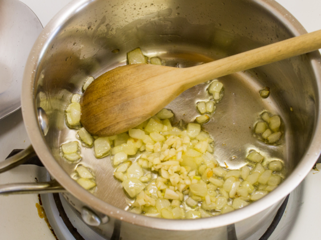 chopped onion and minced garlic in saucepan with olive oil being stirred with a wooden spoon.
