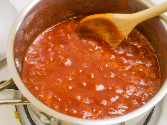 Barbecue sauce simmering in a small saucepan with a wooden spoon.
