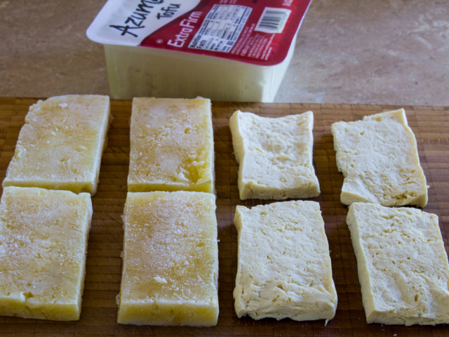 Four slices frozen tofu and 4 slices  of thawed tofu on a cutting board.