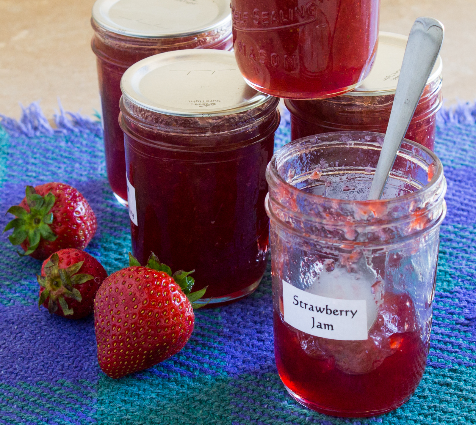 One open jar of strawberry jam with four jars of sealed jam.
