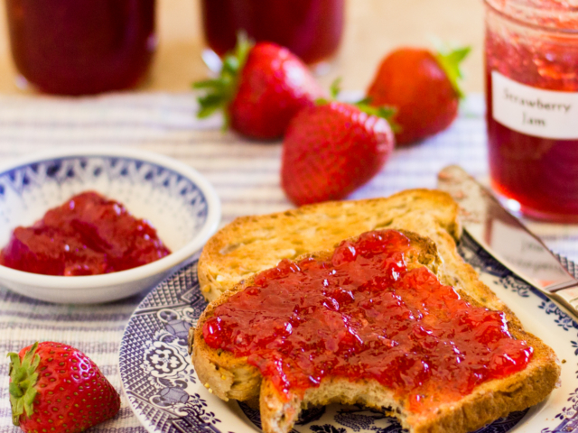 Two slice s of toast with strawberry jam spread on the top slice.