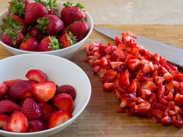 Fresh strawberries in a bowl and chopped strawberries on cutting board.