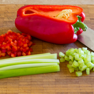 Diced celery and red bell pepper on a cutting board with a knife.