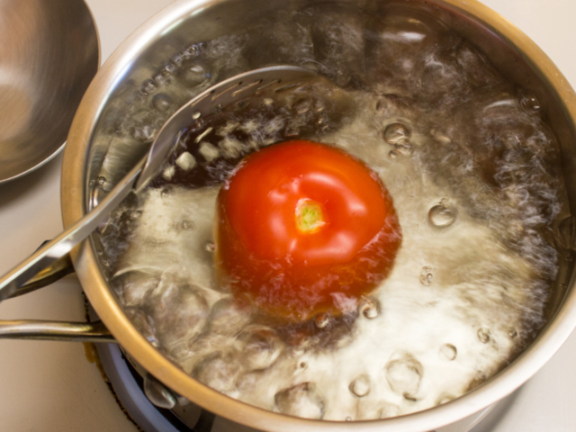 Fresh tomato simmering in small saucepan of water.