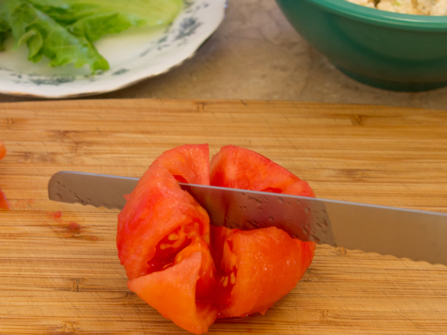 Tomato on cutting board being sliced into wedges.